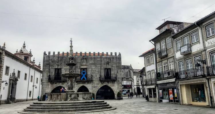 Historisch Portugees plein met fontein en grijsstenen overheidsgebouwen op een bewolkte dag.