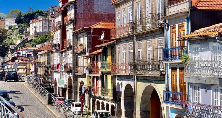 Kleurrijke rij van historische huizen aan de rivier met smeedijzeren balkons onder de felle zon.