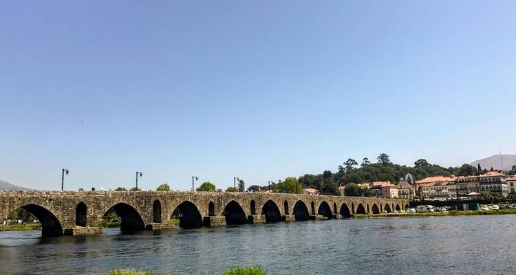 Long pont de pierre de style médiéval enjambant une rivière paisible avec une petite ville sur la rive opposée.