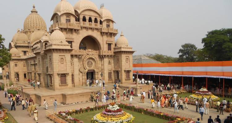Menschenmengen erkunden den kuppelförmigen Sandstein-Tempelkomplex Belur Math, umgeben von bunten Blumenbeeten.