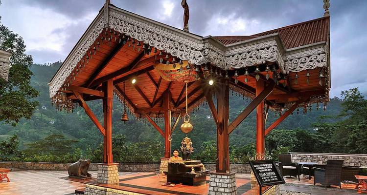 Kunstvoll verzierter offener Pavillon-Tempel, warm beleuchtet vor nebligen bewaldeten Hügeln in der Dämmerung.