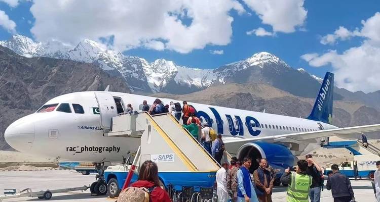 Los pasajeros desembarcan de un avión azul y blanco en un aeropuerto de montaña con picos nevados detrás.