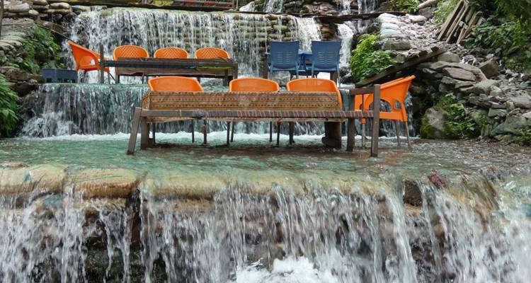 Sillas y mesas de color naranja brillante están ubicadas en medio de un arroyo de montaña en cascada.
