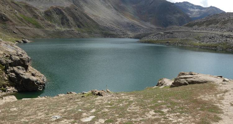 Un tranquilo lago alpino se encuentra en una cuenca rocosa bajo montañas grises y áridas.