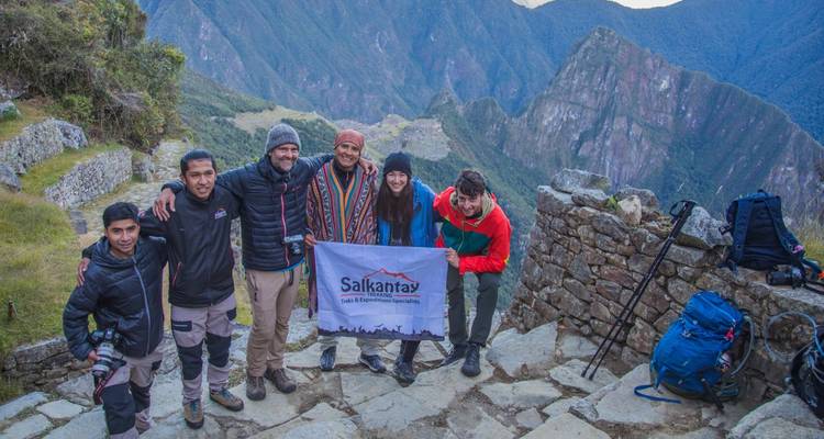 Un groupe de randonneurs pose avec une bannière Salkantay sur une terrasse de pierre surplombant le Machu Picchu.