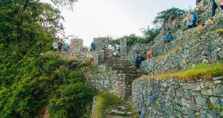Les visiteurs explorent les escaliers et murs de pierre d'un complexe de ruines incas par une journée ensoleillée.