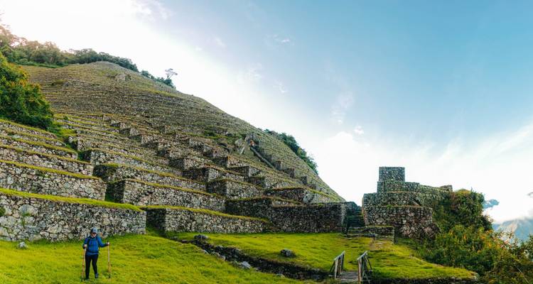 Scène panoramique de terrasses agricoles en pierre et de randonneurs gravissant une colline escarpée de ruines incas sous un ciel bleu
