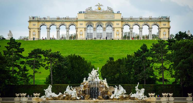 Élégant pavillon Gloriette couronne la colline verdoyante des jardins de Schönbrunn avec la fontaine de Neptune au premier plan