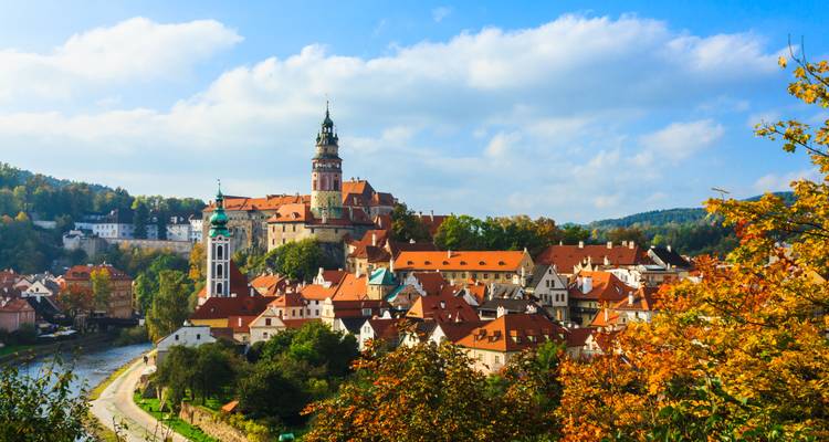 Encantadora ciudad medieval de Cesky Krumlov con torre del castillo y tejados rojos entre árboles otoñales