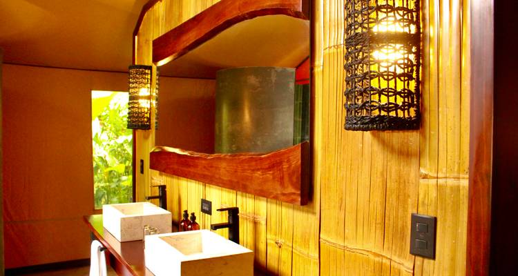 Stijlvolle glamping badkamer met dubbele stenen wastafels, bamboe wanden en warme geweven lantaarnverlichting.