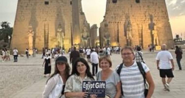 Quatre touristes posant avec un panneau de visite devant l'entrée illuminée d'un temple ancien en grès au crépuscule.