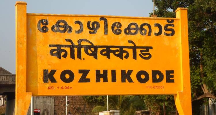 Panneau de gare ferroviaire jaune vif affichant le nom Kozhikode en plusieurs écritures.