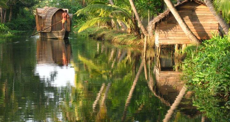 Péniche traditionnelle du Kerala glissant le long d'un étroit canal de backwater bordé de palmiers près d'une hutte en bois.