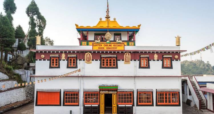 Farbenprächtiges buddhistisches Kloster mit verzierten Fenstern und Gebetsfahnen vor weißen Mauern und hohen Kiefern.