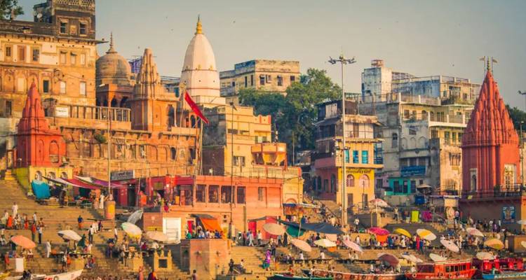 Farbenfrohe Flussufer-Ghats von Varanasi mit historischen Tempeln und lebhaften Marktschirmen unter weichem Nachmittagslicht.