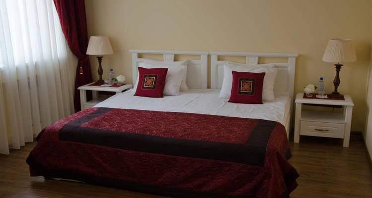 Neat hotel bedroom with large double bed, red accents and warm lighting.