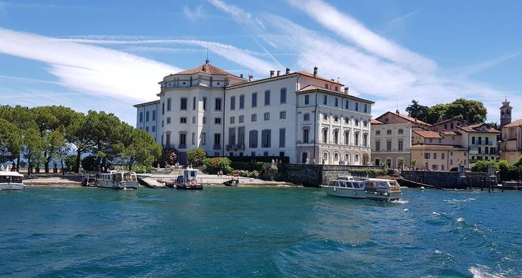 Élégant palais au bord de l'eau et petites embarcations sur le lac Majeur turquoise sous des nuages cirrus striés