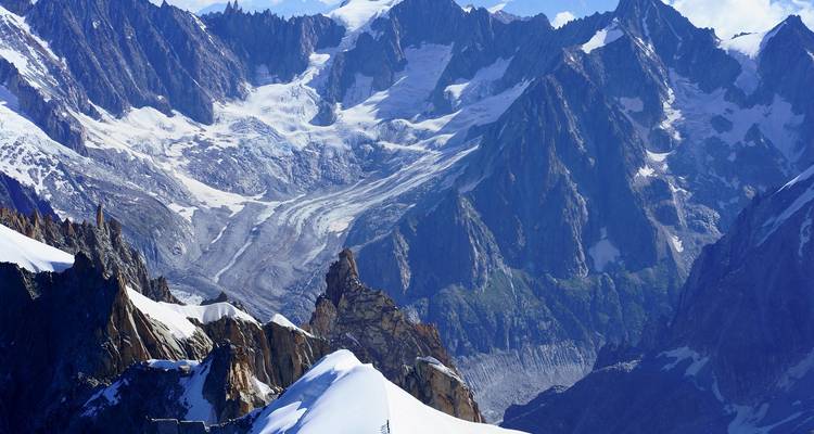 Vue alpine élevée de pics déchiquetés couverts de neige et d'un glacier majestueux sous un ciel bleu dégagé.