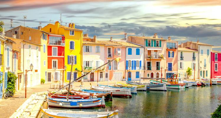 Canal pittoresque bordé de maisons méditerranéennes aux couleurs vives et de petits bateaux de pêche au coucher du soleil.