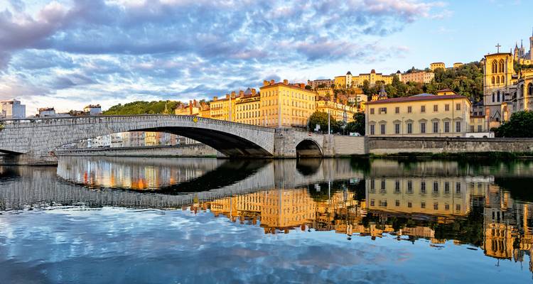 Morning light illuminates classic stone bridge and pastel riverside buildings of Lyon mirrored in the Saône.
