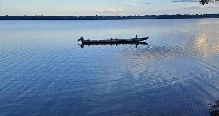 Un petit canoë motorisé glisse sur un immense lac calme, reflétant les nuages légers.