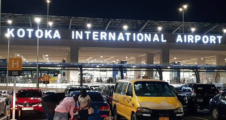 Night view of Kotoka International Airport facade with parked vehicles and illuminated signage.