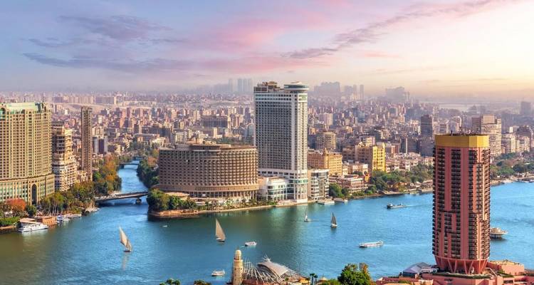 Panoramic sunset view of Cairo skyline with Nile River, high-rise hotels and boats.