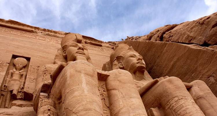 Primer plano en ángulo bajo de las grandes estatuas de Ramsés II en Abu Simbel contra un cielo azul.