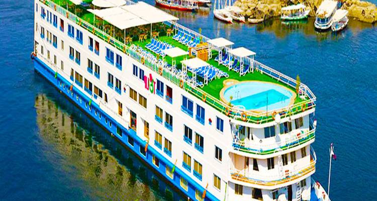 Un barco de crucero por el Nilo de varios pisos pintado de colores brillantes con una piscina en la azotea navega por aguas azules tranquilas.