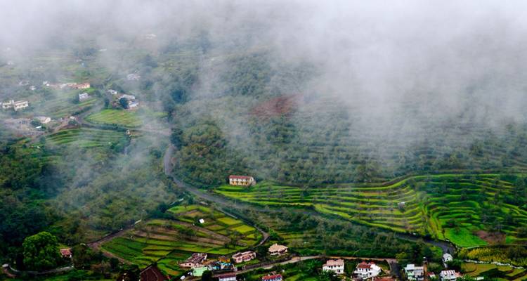 Mist die over terrasvormige groene heuvelflanken en verspreide dorpshuizen drijft