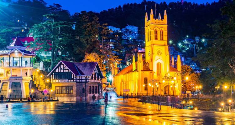Shimla's Christ Church gloeiend onder nachtverlichting op een nat reflecterend plein