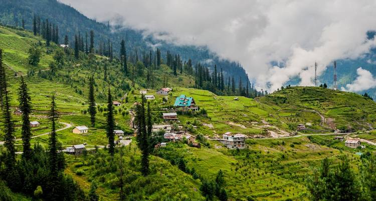 Weelderige groene vallei bezaaid met huizen en hoge dennen tegen een mistige bergachtergrond