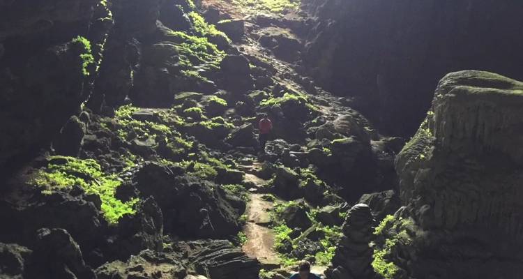 Entdecker, die zwischen moosbewachsenen Felsen in einer schwach beleuchteten Höhle wandeln.