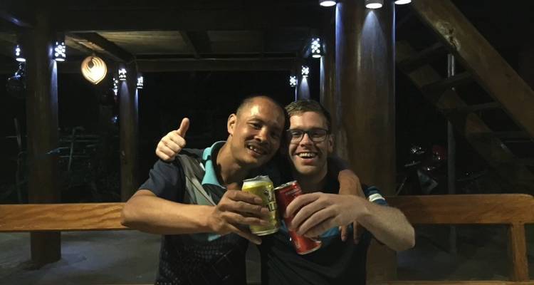 Zwei Freunde stoßen mit Dosen in einem hölzernen Pfahlbau in der Nacht an.