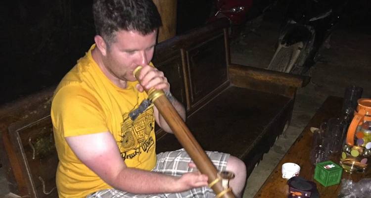 Reisender sitzt auf einer Holzbank und experimentiert mit einer traditionellen Bambusflöte.