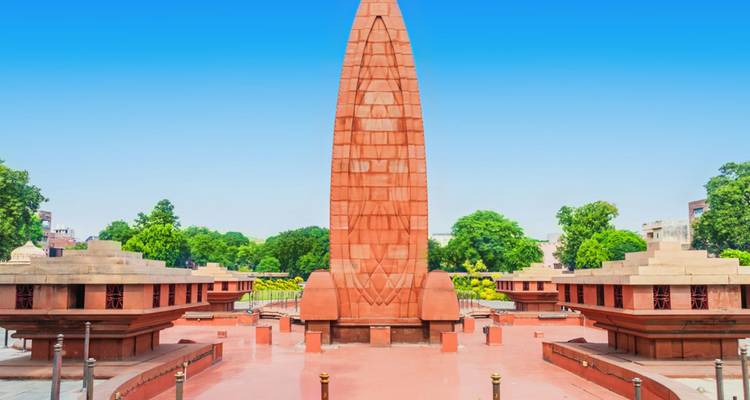 El alto obelisco rojo del memorial de Jallianwala Bagh contra un cielo azul brillante.