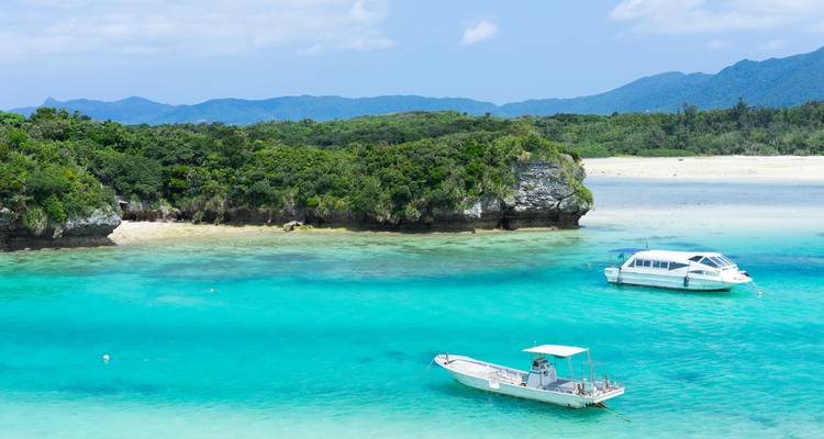 Eau turquoise cristalline et bateaux à l'ancre dans la baie de Kabira avec des îlots luxuriants et des montagnes