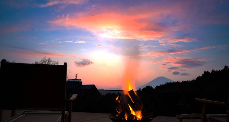Feu de camp qui flambe sur une terrasse au coucher du soleil avec le mont Fuji silhouetté contre un ciel coloré