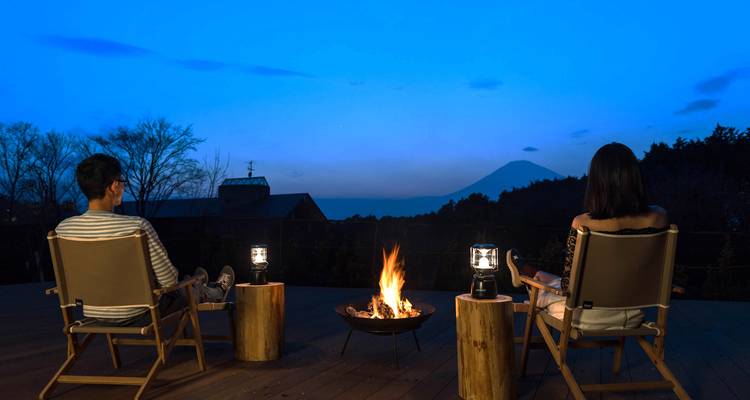 Deux personnes sont assises près d'un foyer sur une terrasse au crépuscule avec le mont Fuji au loin