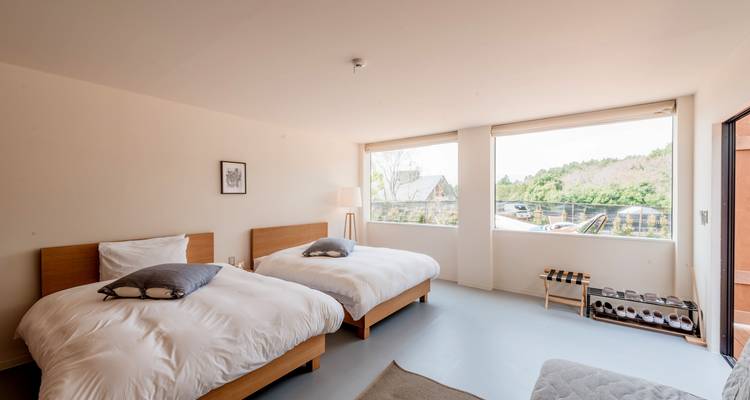 Chambre lumineuse et minimaliste avec lits jumeaux et de grandes fenêtres donnant sur des collines boisées