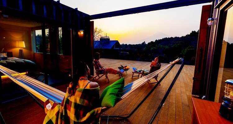 Les voyageurs se détendent dans des hamacs sur une large terrasse en profitant de la vue du coucher de soleil vers le mont Fuji