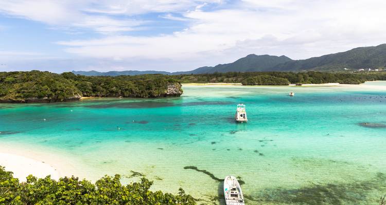 Lagon turquoise avec bancs de sable coralliens et promontoires boisés contre des montagnes lointaines