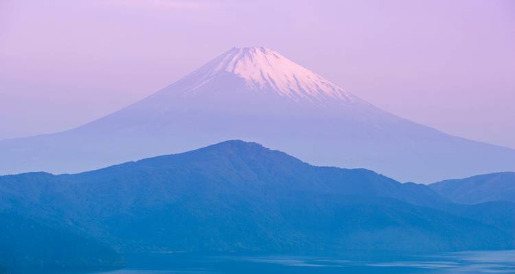 Le mont Fuji s'élève dans la lumière pastel de l'aube au-dessus des crêtes brumeuses