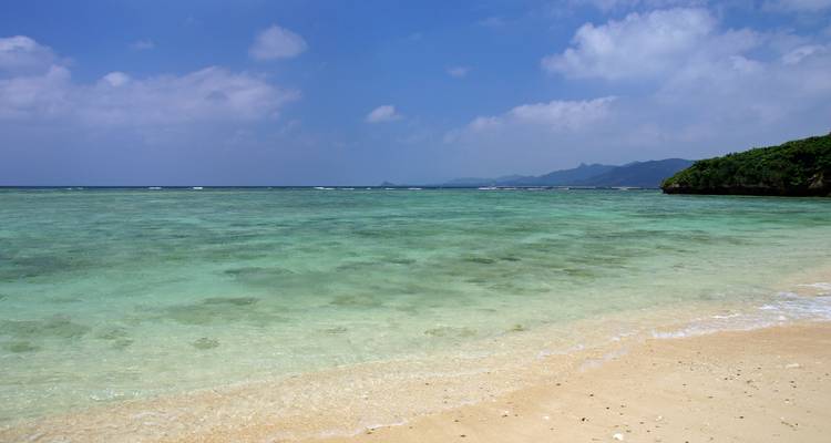 Une mer turquoise tranquille lèche une plage de sable silencieuse sous un ciel légèrement tacheté de nuages