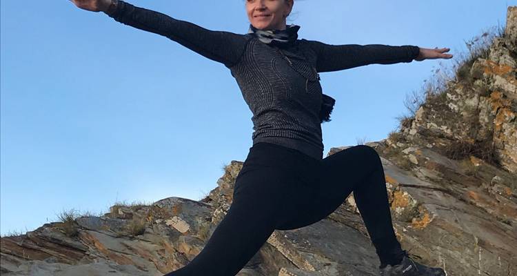 Un voyageur pratique une pose de yoga énergique sur un affleurement rocheux sous un ciel dégagé