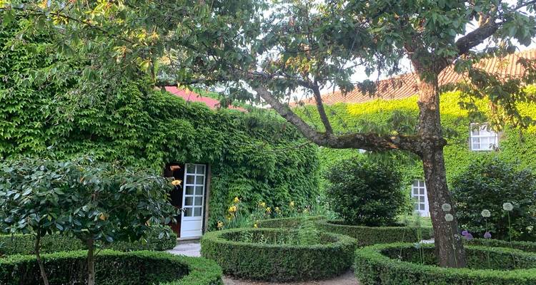 Gepflegter Garten mit kreisförmigen Buchsbaumhecken, Bäumen und efeubedeckten Mauern um eine weiße Tür