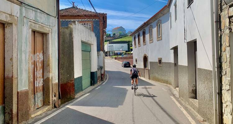 Cycliste descendant une rue étroite bordée de maisons portugaises traditionnelles aux façades délavées.