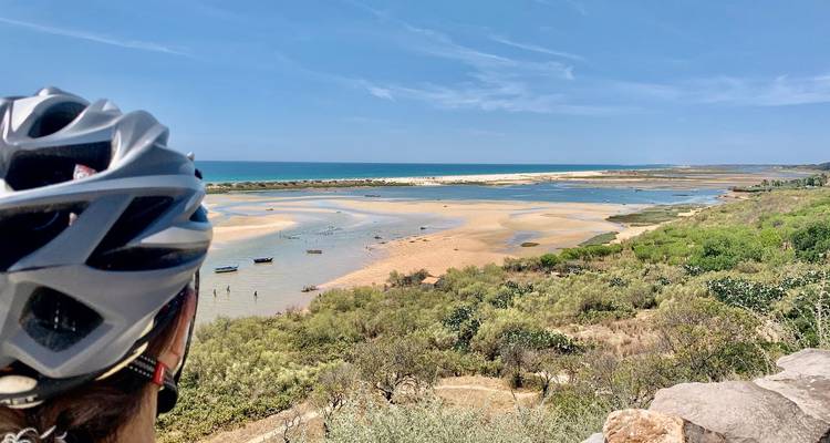 Motorradfahrer mit Helm blickt über eine weite Gezeitenlagune und Sandflächen, die auf den Atlantik treffen