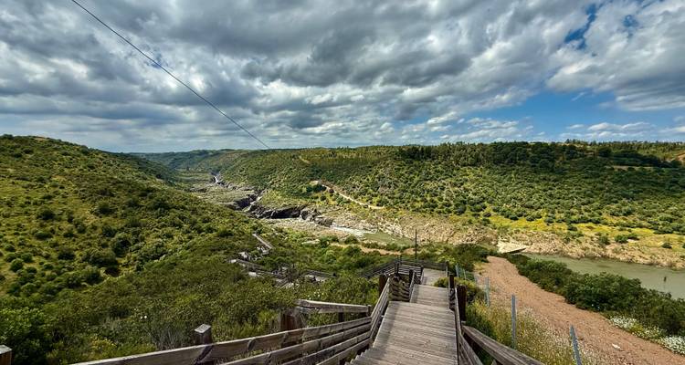 Holztreppe führt hinab zu einer zerklüfteten Flussschlucht unter einem dramatischen bewölkten Himmel