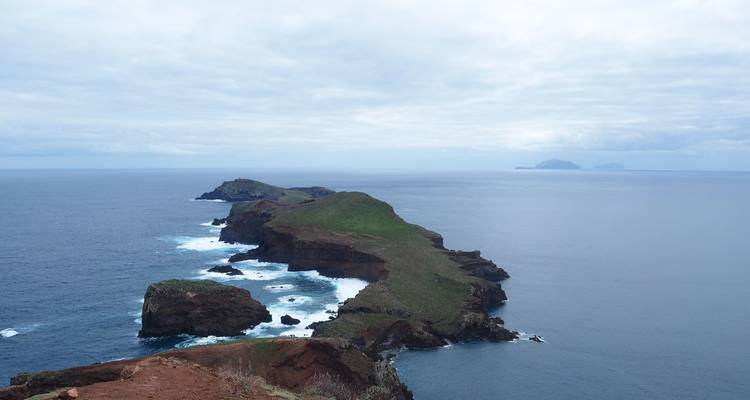 Lange schmale Halbinsel aus roten Klippen erstreckt sich unter einem bewölkten Himmel in den Atlantik